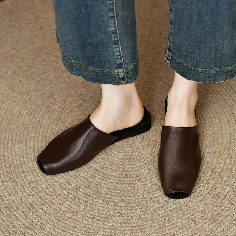 Mule feminina marrom de couro com bico coberto, solado preto, usada com calça jeans