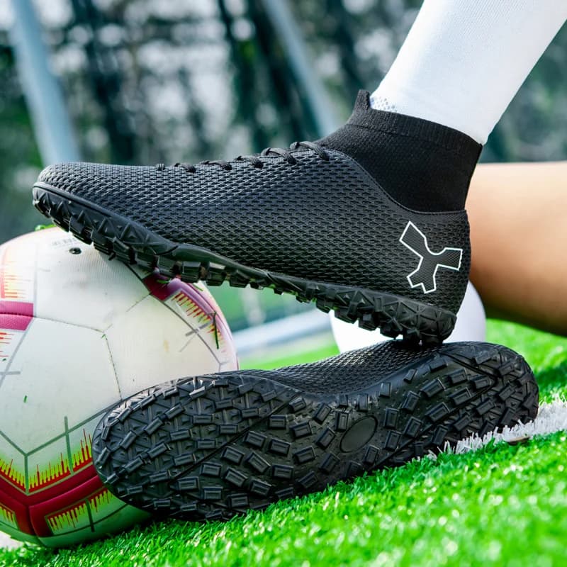 Chuteira society preta com cano elástico e solado de borracha antiderrapante em campo de futebol