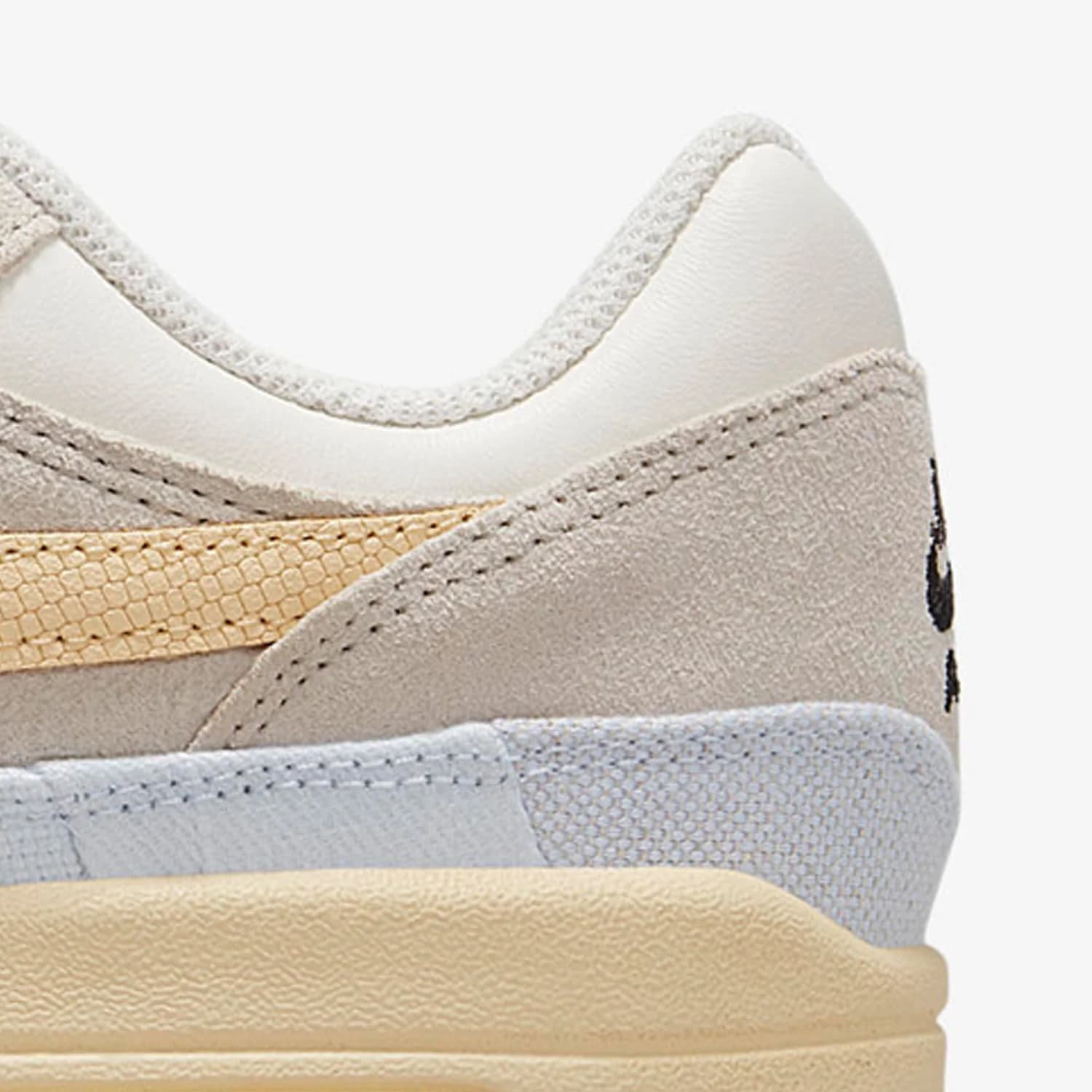 Parte traseira do tênis Nike Air Max 1 feminino em tons off-white, cinza e bege com acabamento em camurça