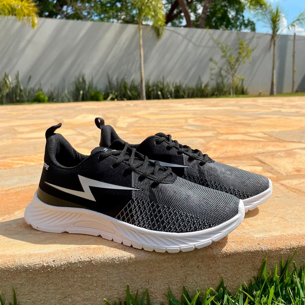 Tênis esportivo unissex preto e branco com design de grade, em pé sobre uma superfície de pedra