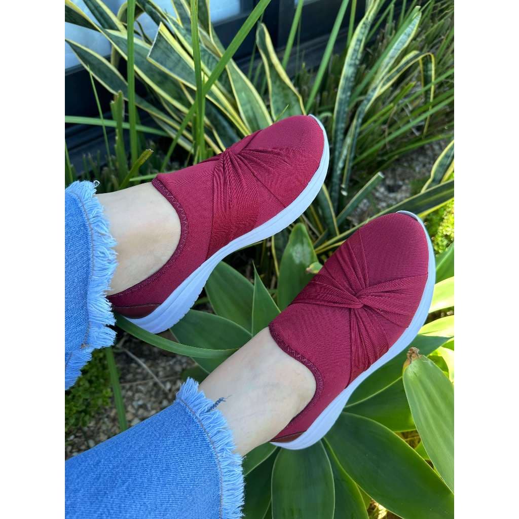 Tênis feminino vermelho com calce fácil, estilo casual e esportivo, sobre fundo verde de plantas