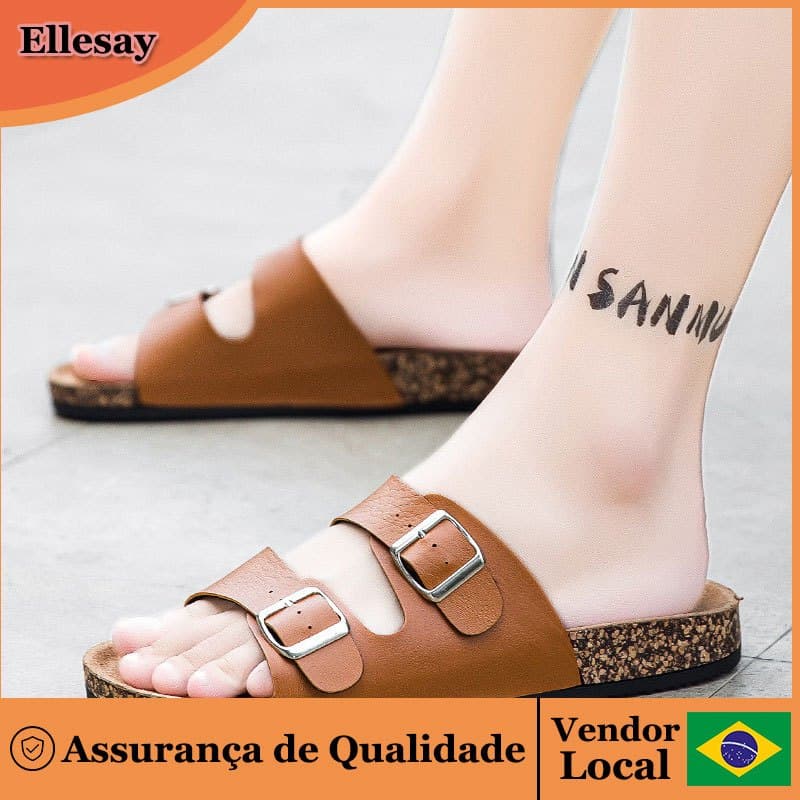Sandálias masculinas marrom com fechos de fivela, solas texturizadas, design de dedos abertos, pés de uma pessoa, fundo cinza, tatuagem no braço, marca Ellesay