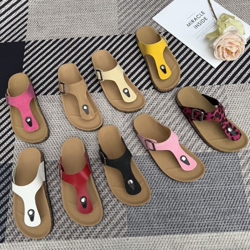 Chinelos de tamanho grande em várias cores - amarelo, rosa, branco, vermelho, preto e marrom - dispostos em um fundo listrado cinza e preto.