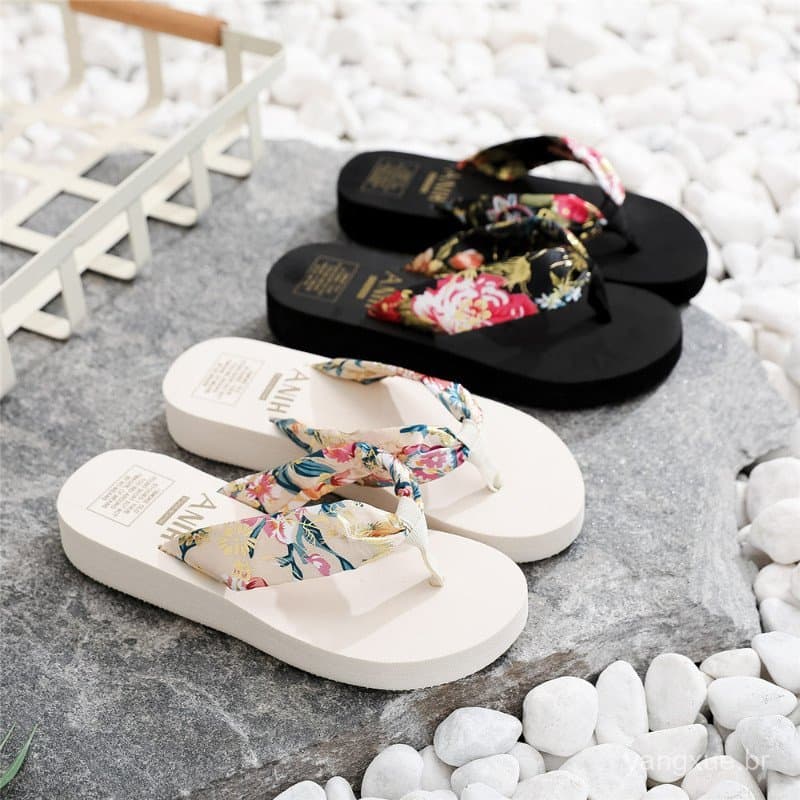 Chinelos femininos estilo boêmio de verão com tira floral, dois pretos e um branco, sobre pedras brancas