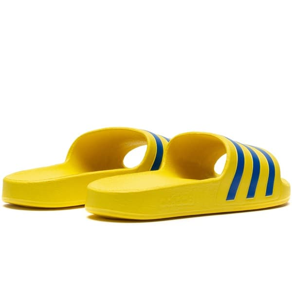 Par de Adidas Adilette Aqua Slippers, amarelo com listras azuis, mostrando furos laterais.