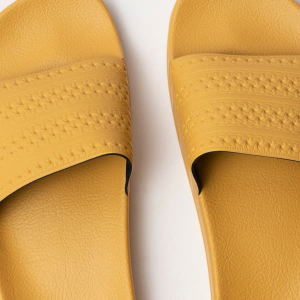 Adidas Originals Adilette flip flops amarelas mostrando a textura e design das tiras.
