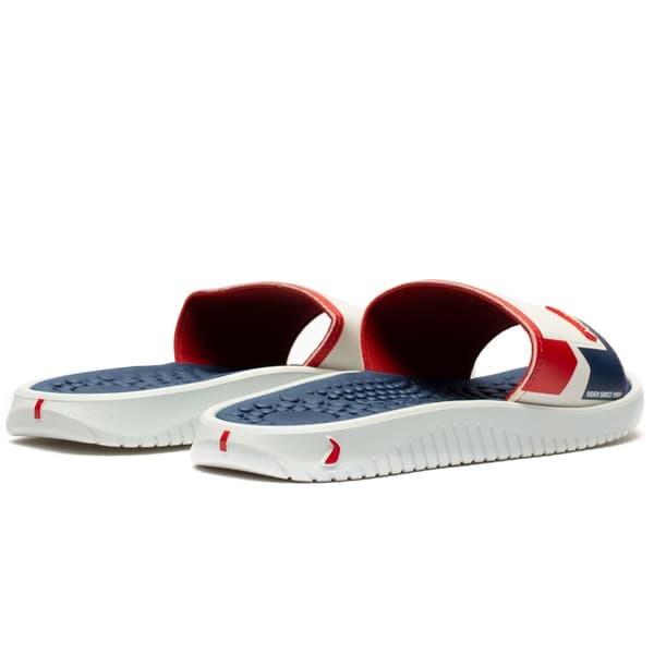 Sapatilha Rider Pump II Slide Slipper com sola pontilhada, detalhes em azul e vermelho.