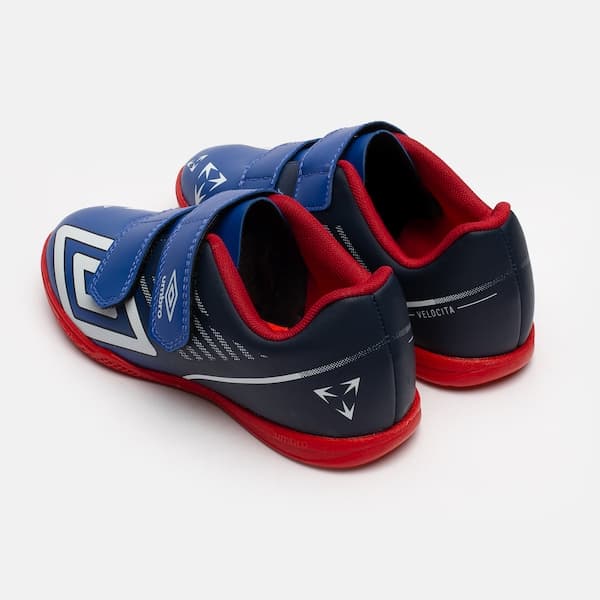 Detalhe de chuteira futsal infantil Umbro Velocita, azul e vermelho, com sola vermelha.
